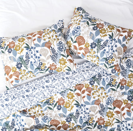 close up of a blue green gold quilt set with abstract flowers with matching shams that reverses to a ditsy foliage pattern