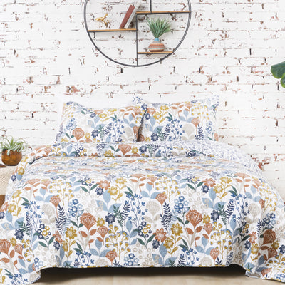 blue green gold quilt set with abstract flowers in front of a whitewashed brick wall