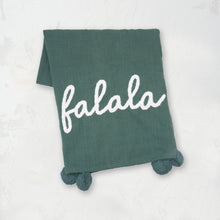 green woven throw with pom pom edges and the word falala in white