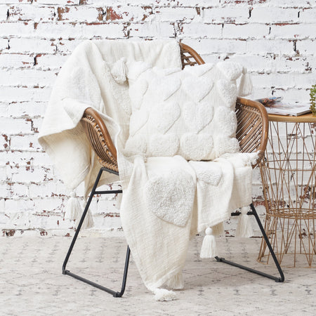 white pillow with a heart tufted pattern and fringed edges on a chair with a matching throw