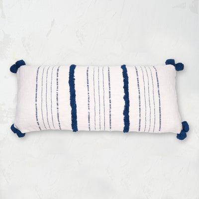 woven white pillow with dark blue pom pom edges and tufting 