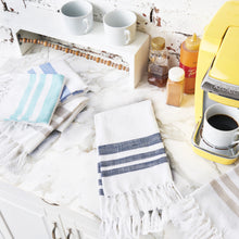 woven kitchen towel with stripes on a white background layered on a marble kitchen countertop and surrounding by mugs and a coffee maker