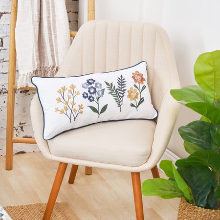 Pillow embroidered with foliage and abstract flowers on a white background with a blue trim on a chair